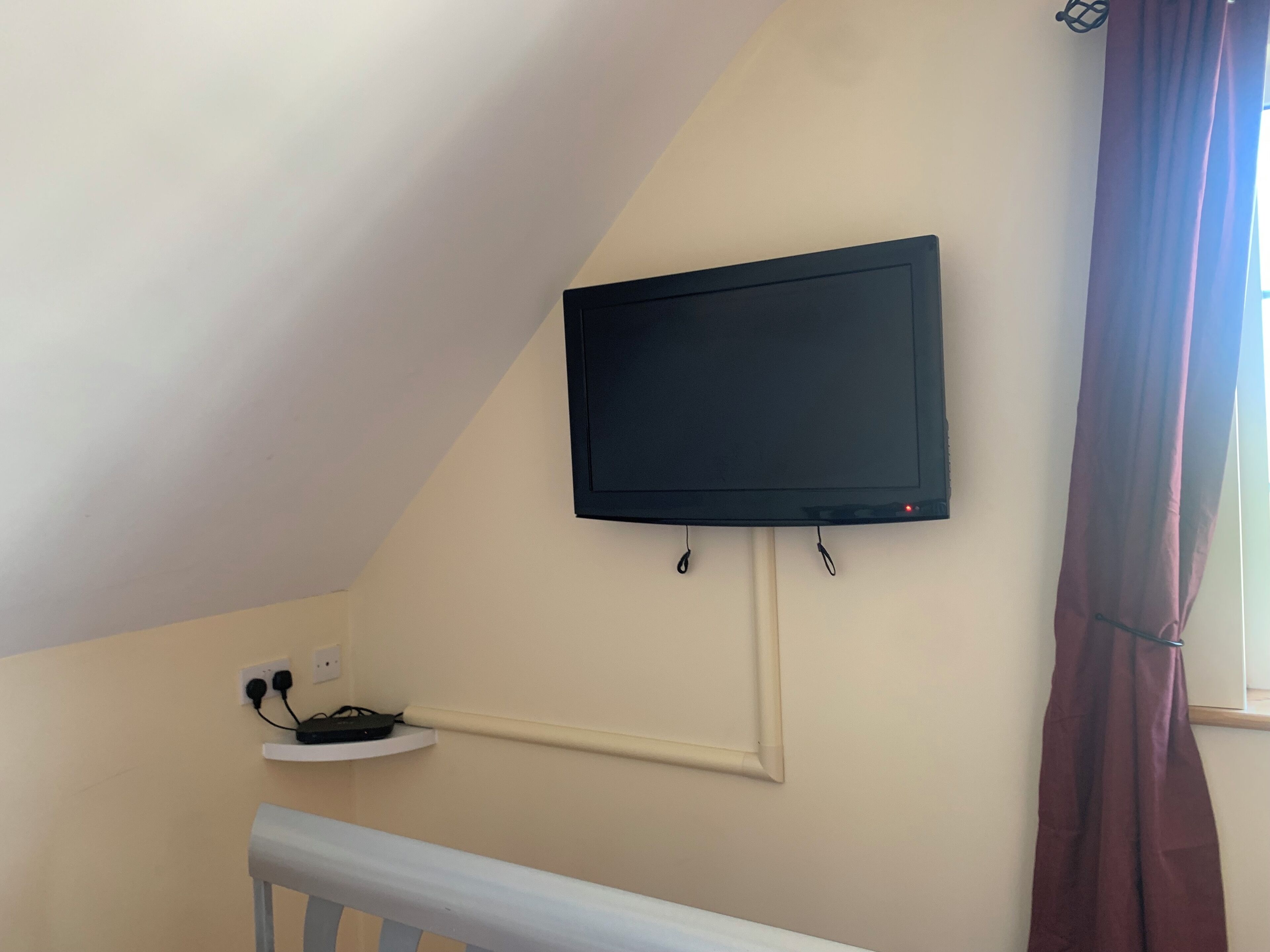 Een televisie aan een muur bevestigd, met een kabel die naar een stopcontact daaronder loopt.
