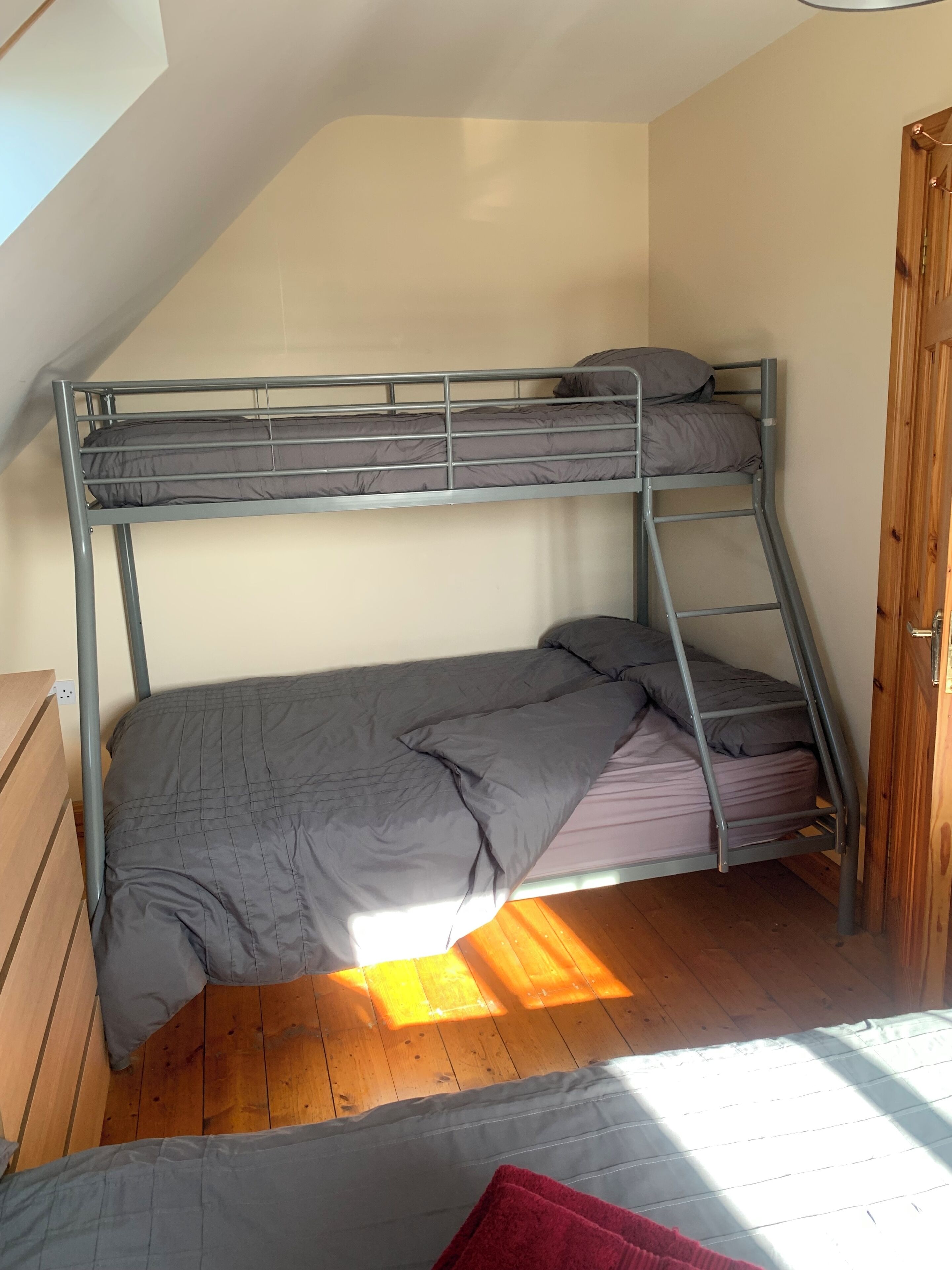 A bunk bed with grey bedding in a room with wooden flooring and a sloped ceiling.