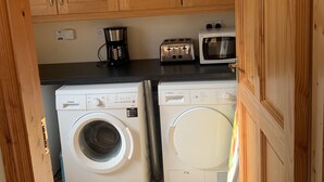 Eine kompakte Küche mit Holzausstattung, einer Kaffeemaschine, einem Toaster und zwei Waschmaschinen mit Frontlader.