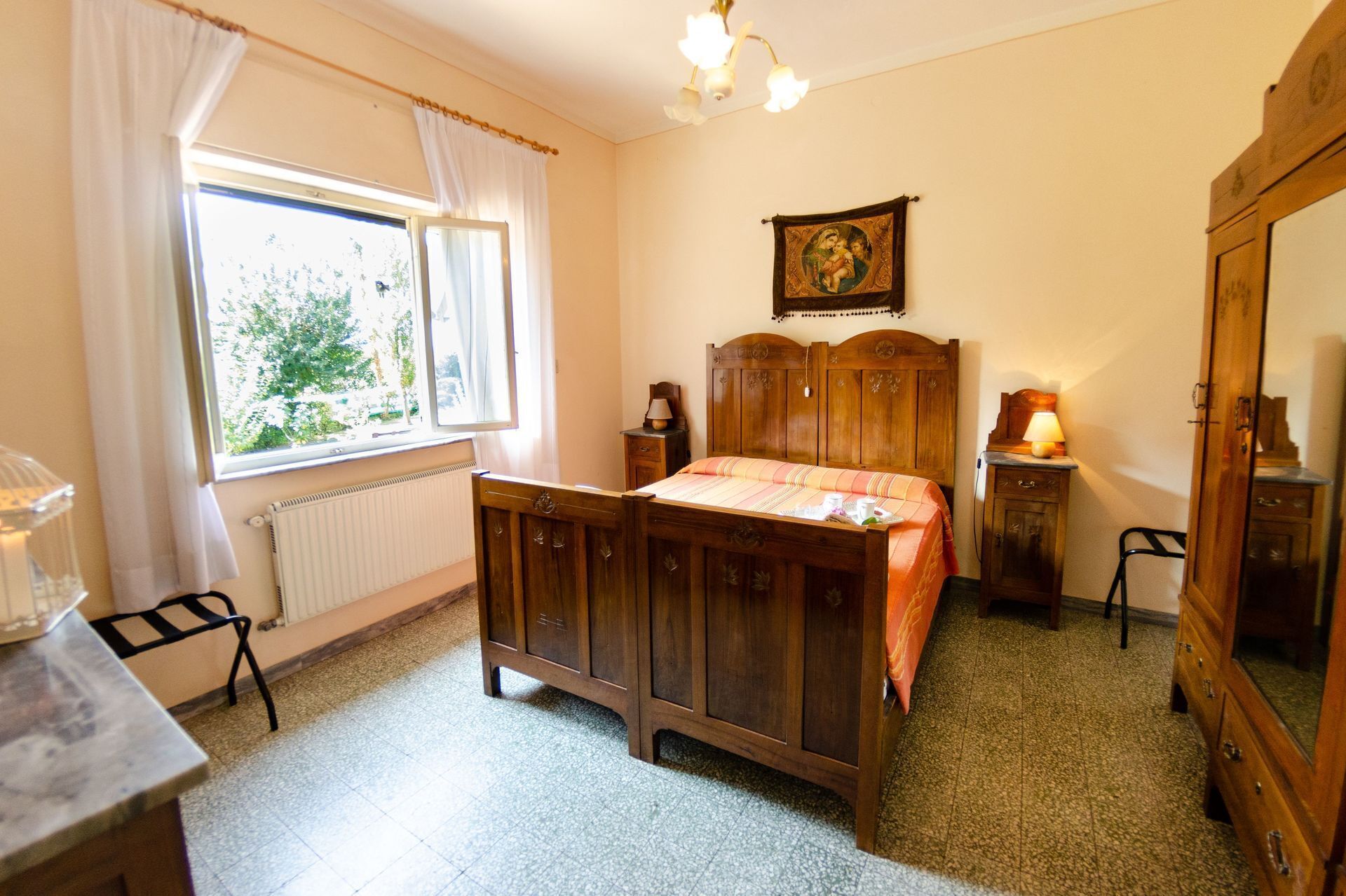 Une chambre à coucher avec un lit en bois, une table de chevet, une commode, une fenêtre avec des rideaux et un radiateur.