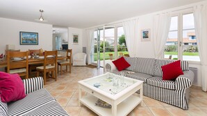 A living room with striped sofas, a glass coffee table, and a dining area with wooden furniture.