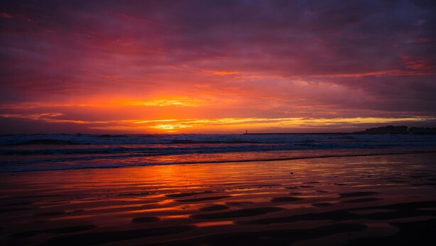 A beach at sunset with waves and a cloudy sky.