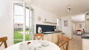 A modern kitchen with a large window, a coffee machine, and a dining area with chairs and a table set for four.