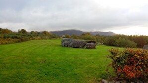 Ein grasbewachsenes Feld mit großen Felsen und einem Haus im Hintergrund.