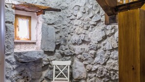 A stone-walled room with a wooden chair, a small window, and a tiled floor.