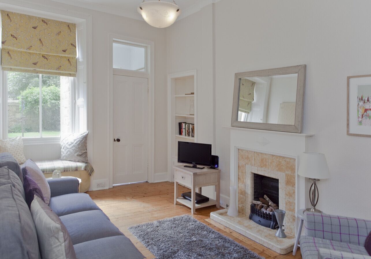 A living room with a sofa, a television on a stand, a fireplace, and a bookshelf.