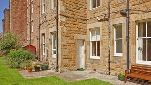 A stone building with multiple windows and a small garden area with a bench. - Main Door Apartment in an enviable location (Edinburgh)