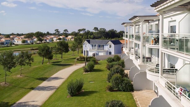 Un hotel moderno con fachada blanca, varios balcones y vistas a una zona residencial con casas y vegetación.