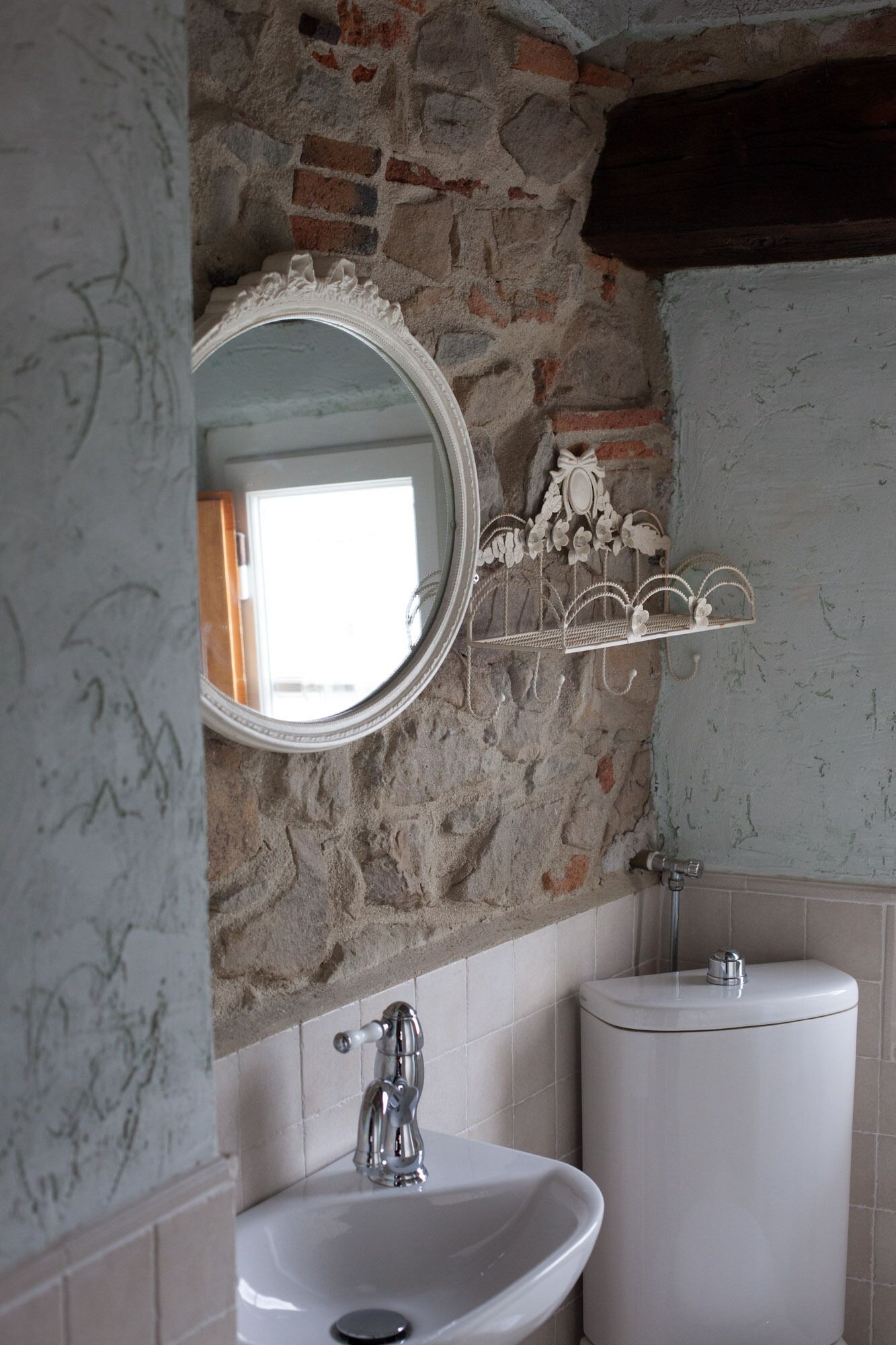 A bathroom with a stone wall, a white sink, a mirror, and a toilet.
