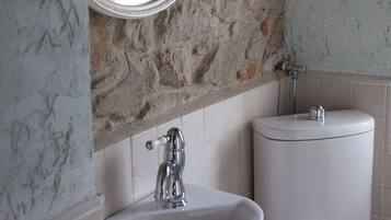 A bathroom with a stone wall, a white sink, a mirror, and a toilet.