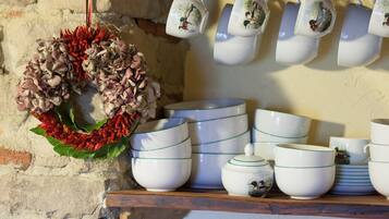 A rustic kitchen with a wooden shelf displaying white ceramic mugs, bowls, and plates.