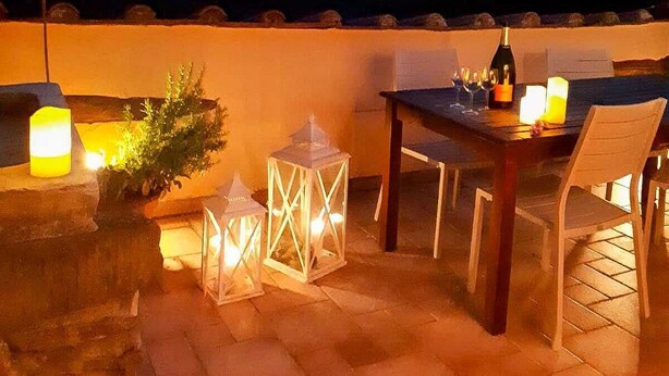 Een terras buiten met een eettafel, omringd door lantaarns en kaarsen, met uitzicht op een bergachtig landschap.