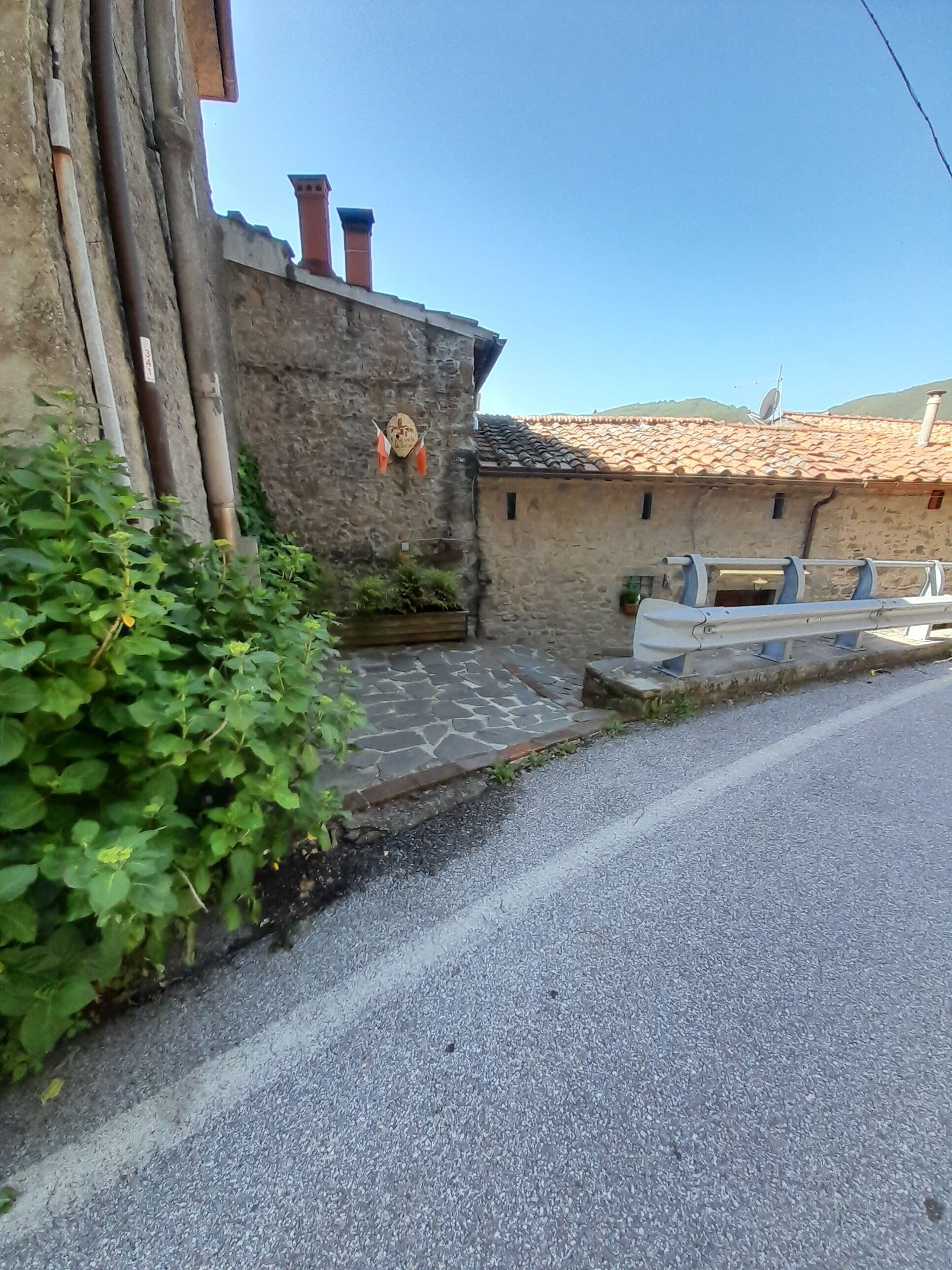 Une rue étroite bordée d’immeubles en pierre, avec une chaussée pavée et de la verdure.