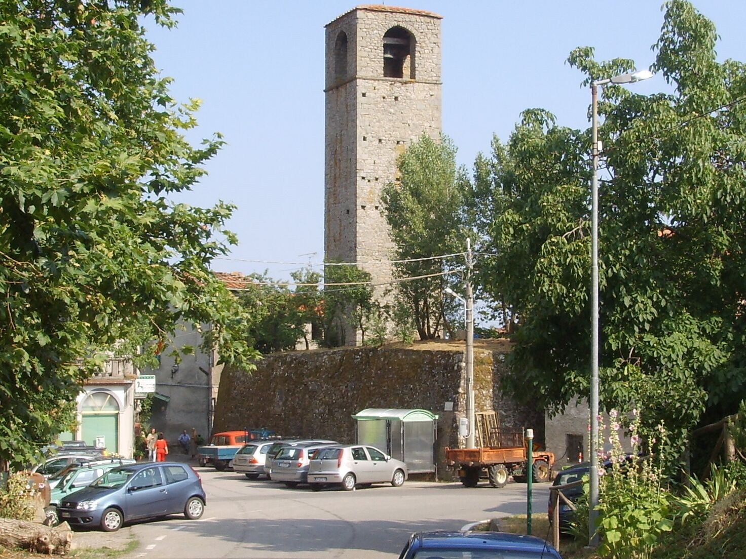 Un estacionamiento con varios coches, una alta torre de piedra y un edificio con techo verde.