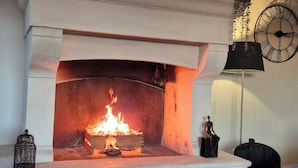 A fireplace with a fire, a glass table with a bottle and glass, and a clock on the wall. - In PROVENCE, Facing LUBERON, A LITTLE CORNER OF PARADISE, PRIVATE VILLA FOR 6 Pers (Cabrières-D'avignon)