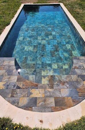 Una piscina rectangular con fondo de azulejos y borde de piedra.