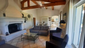 A living room with a fireplace, sofa, and coffee table. There is a dining area in the background with a table and chairs. - In PROVENCE, Facing LUBERON, A LITTLE CORNER OF PARADISE, PRIVATE VILLA FOR 6 Pers (Cabrières-D'avignon)