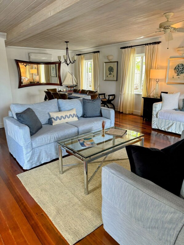 A living room with a light blue sofa, a glass coffee table, and a grey armchair. There is a wooden ceiling and a ceiling fan.