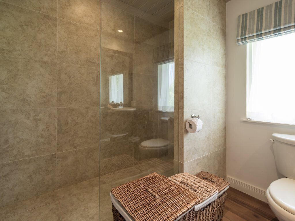 A bathroom with a glass-enclosed shower, a toilet, and a wicker basket.