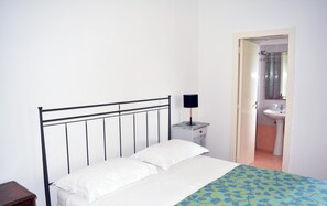 A bedroom with a bed, a bedside table, a lamp, and a bathroom visible through an open door. - apartment/ flat - Casarano (Casarano)