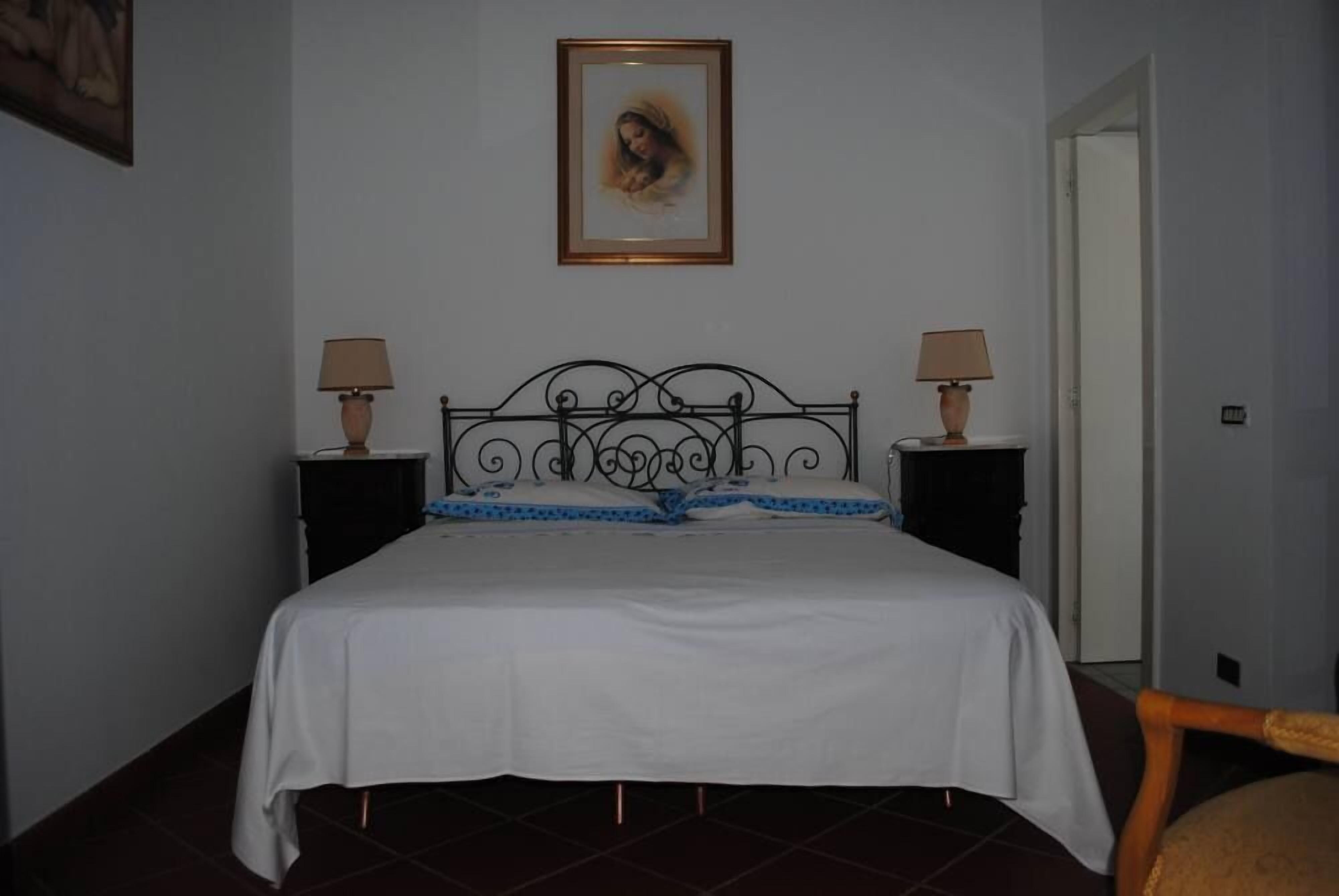 A bedroom with a bed, two bedside tables, a lamp on each table, a framed picture on the wall, and a chair in the corner.