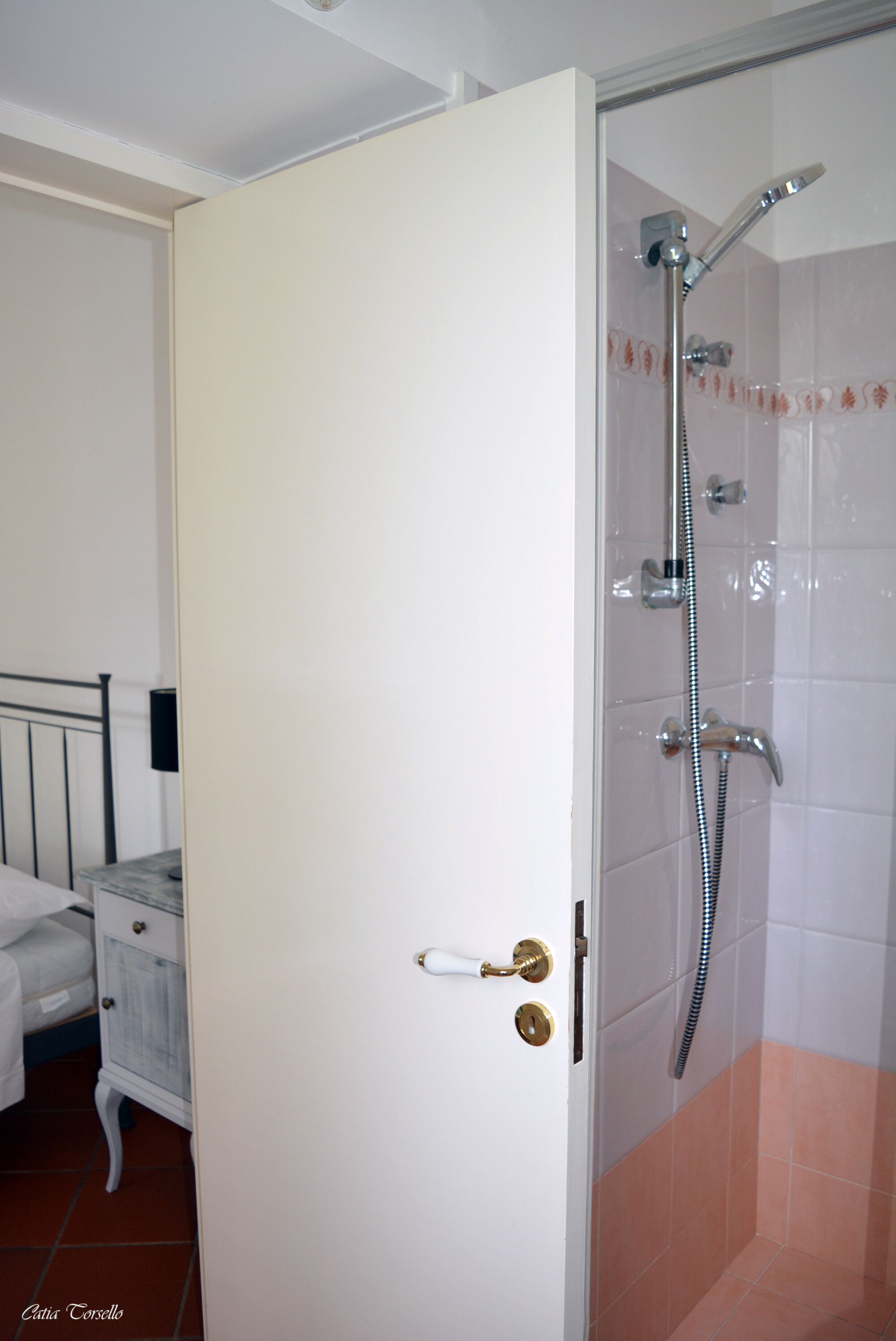 Un baño con ducha, una puerta blanca y una mesita de noche con lámpara.