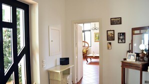 Un pasillo con una puerta blanca, una mesita con una lámpara y un espejo a la derecha. Hay cuadros enmarcados en la pared y una silla al fondo.