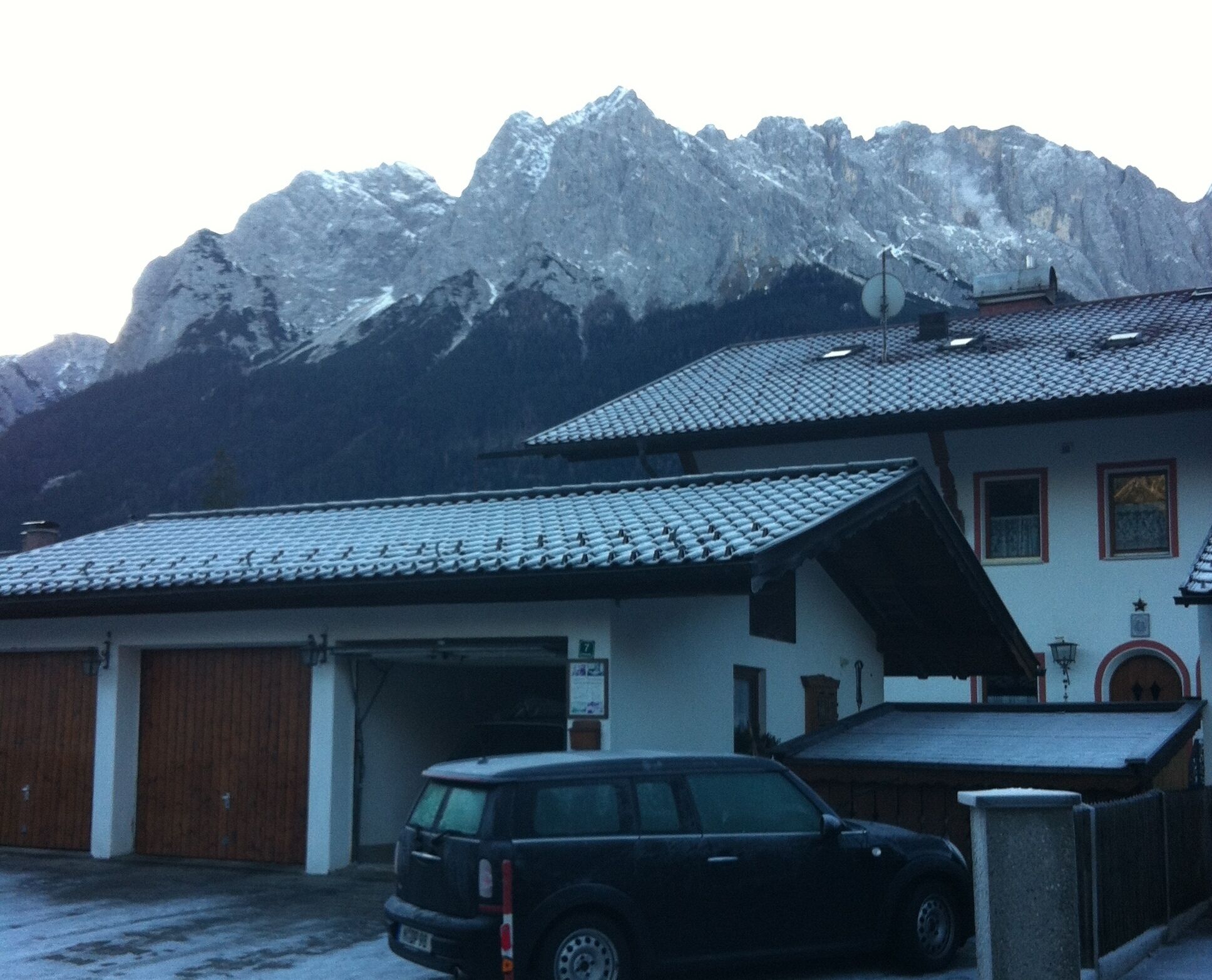 A building with a garage, a parked car, and snow-covered mountains in the background.