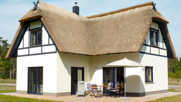 A house with a unique thatched roof, a front porch with a table and chairs, and a chimney. - apartes holiday house with fireplace and sauna invites you to a relaxing holiday (Zirchow)