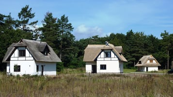 Drei traditionelle Häuser mit Strohdächern in einer grünen Wiese.