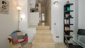 A modern interior with a staircase leading to a kitchen area, a glass table, and a bookshelf with books and decorative items. - Near La Caleta. Ascenseur.WIFI (Cádiz)