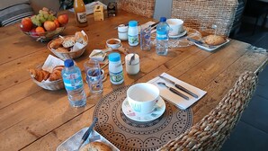 Une table de salle à manger en bois, sur laquelle on trouve une variété d’aliments, notamment du pain, des fruits et une bouteille d’eau.