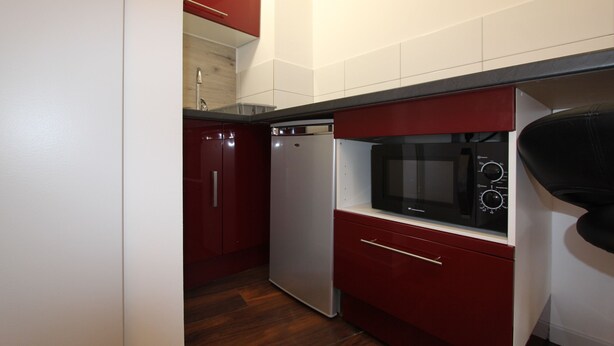 Una cocina compacta con muebles rojos, microondas integrado y lavavajillas.