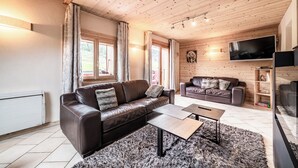 A cozy living room with two leather sofas, a coffee table, and a TV mounted on the wall. - Beautiful 4-star duplex apartment available for rent in the Centre des Gets (Les Gets)