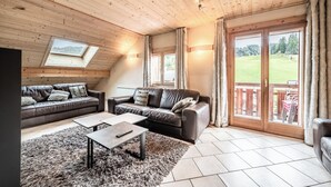 A cozy room with two leather sofas, a coffee table, and a large window offering a view of a green landscape. - Beautiful 4-star duplex apartment available for rent in the Centre des Gets (Les Gets)