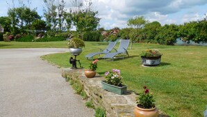 A garden with a paved path, two lounge chairs, and potted plants along the edge. - Unique all comfort Longere, close to the sea of Iroise (Ploumoguer)