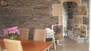 A dining area with a stone wall, wicker chairs, a wooden table, and a vase of flowers. - Unique all comfort Longere, close to the sea of Iroise (Ploumoguer)