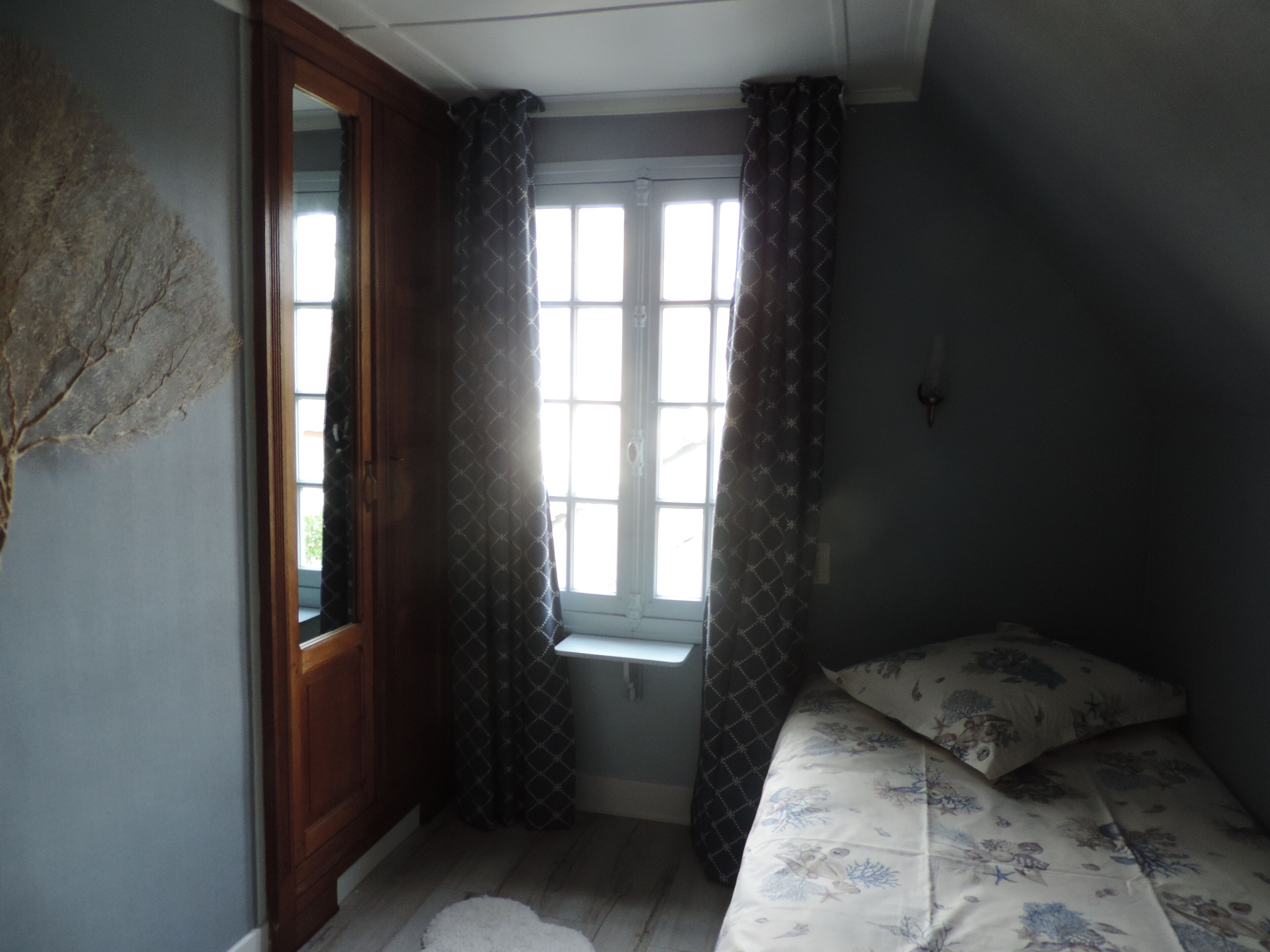 A room with a bed, a window with curtains, a door, and a wall with a textured pattern.