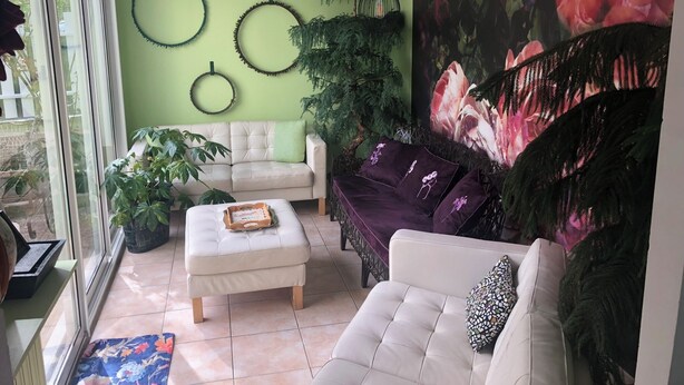 Ett vardagsrum med en vit soffa, en lila soffa och en vit fåtölj. Det finns tre runda väggdekorationer och en stor tavla med blommotiv.