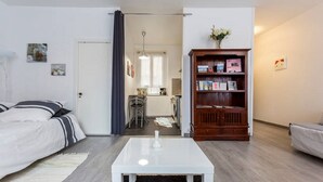 A compact living space with a bed, a white coffee table, a bookshelf, and a kitchen area visible through an open door. - Bordeaux Hyper Center ville Rue Courbin renovated, cozy and bright (Bordeaux)