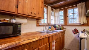 A kitchen with wooden cabinets, a microwave, a sink, and a window with curtains. - Romantic & private cabin on Rogue River, 1 hr from Crater Lake (Trail)
