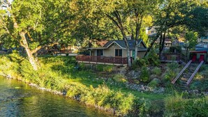 A lakeside cabin with a deck, surrounded by lush greenery and a clear view of the water. - Romantic & private cabin on Rogue River, 1 hr from Crater Lake (Trail)