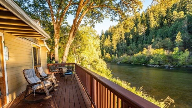 A wooden deck with rocking chairs and a table overlooking a river, surrounded by trees. - Romantic & private cabin on Rogue River, 1 hr from Crater Lake (Trail)
