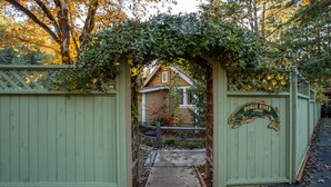 A rustic wooden gate with a sign reading "Rogue River Trail Marker" leading to a house with a visible porch and a small garden. - Romantic & private cabin on Rogue River, 1 hr from Crater Lake (Trail)