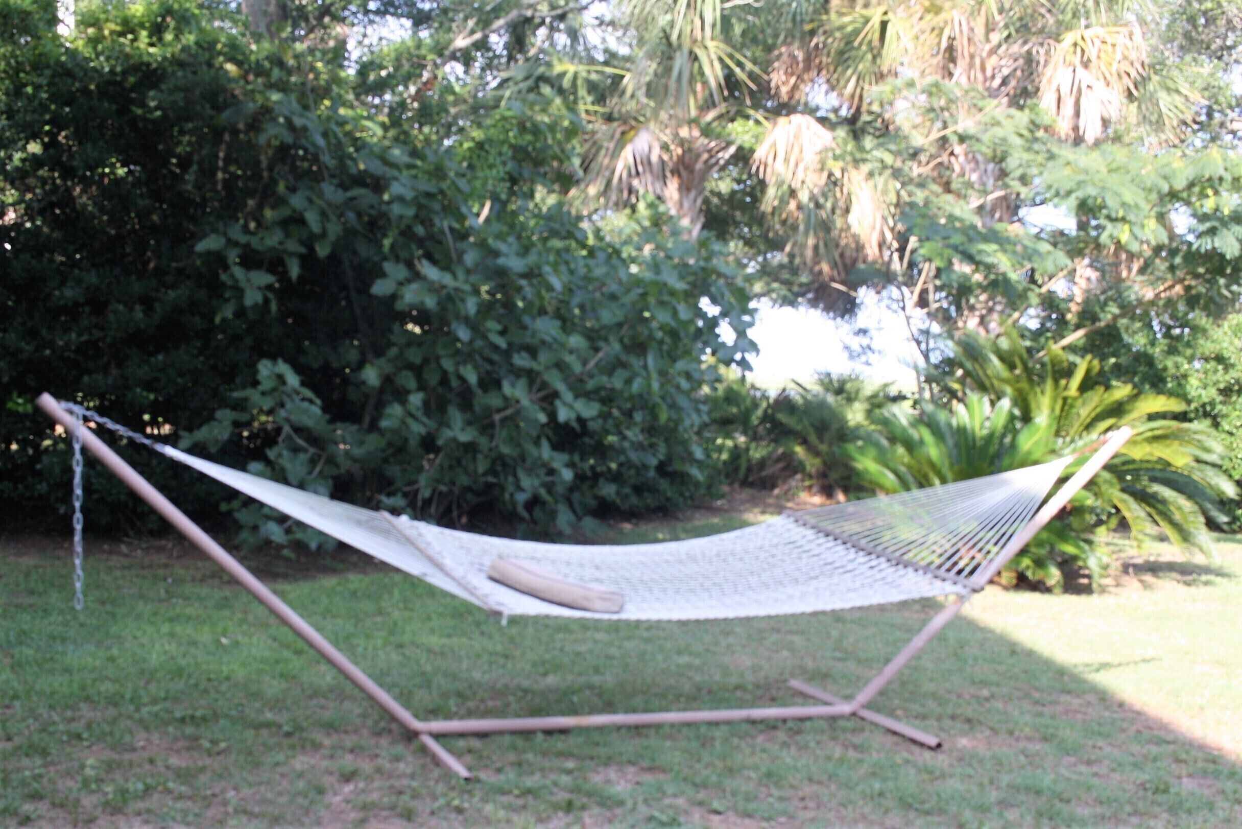 Un hamac installé dans un espace herbeux, avec un feuillage dense en arrière-plan.