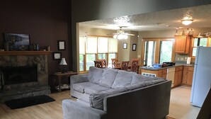 A living room with a grey sofa, a fireplace, a dining area with wooden chairs, and a kitchen with wooden cabinets and a refrigerator. - Cabin on Dale Hollow Lake - Hike to lake (Monroe)