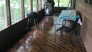 A covered porch with a wooden floor, a table with chairs, a grill, and a water cooler. - Cabin on Dale Hollow Lake - Hike to lake (Monroe)