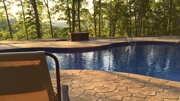 A pool area with a stone patio, a lounge chair, and a wooden bench. - Cabin on Dale Hollow Lake - Hike to lake (Monroe)