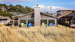 Et moderne hus med en markant skorsten, store vinduer og udendørs siddepladser med Adirondack-stole.
