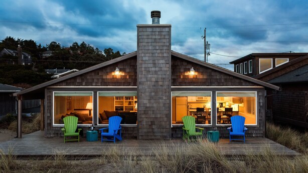 Et moderne hus med en stor skorsten, to store vinduer og en terrasse med fire Adirondack-stole.